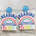 Regenbogen und Buchmuster Holzohrringe mit blauen Glitzersteckern auf Steinhintergrund - Regenbogen Buch Muster