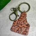 Nahaufnahme von Vintage-Leder-Schlüsselanhänger mit Prägung und bronzenen Metallteilen - Braun Botanisch Geprägt