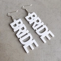 Detailaufnahme der weißen Acryl BRIDE Buchstaben Ohrringe mit Metallhaken auf grau - Silberner Haken - Weiß