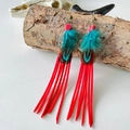 Detail of red tassel earrings with peacock feathers and copper hooks on wood - True Red