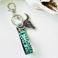 Close-up of western leather keychain with turquoise floral embossing and rhinestone bull head - Black Brown Faux Fur Bull Head