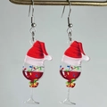 Detailed close-up of acrylic Christmas wine glass earrings with Santa hat and bell charms - Red Wine Glass Xmas Hat