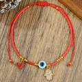 Detail van rood koordarmband met gouden Hand van Fatima en boze oog bedeltjes op hout - Hamsa Hand Hanger Stijl (ZJ15143)
