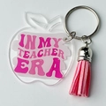 Détail d'un porte-clés pomme en acrylique avec pompon rose et texte In My Teacher Era - Style Typographie Rose - Gland Rose