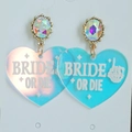 Nahaufnahme von herzförmigen Acryl-Ohrringen mit schillerndem Effekt und Bride or Die Text - Holographisches Herz Braut Oder Stirb