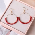 Détail de boucles d'oreilles bohèmes en perles rouges avec fil doré dans une boîte - Rouge