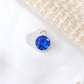 Dettaglio ravvicinato di un ciondolo con pietra blu sfaccettata e cornice in metallo argento - Diametro 6mm / Settembre (P1243)
