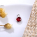 Macro detail of 6mm red birthstone charm with silver-plated copper edge and hanging loop - 6mm / Silver - Red (January)