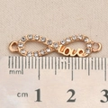 Makroaufnahme von Gold-Infinity-Love-Anhänger mit Strasssteinen und Größenvergleich - Love Unendlichkeits Stil (P2576)