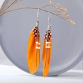 Bohemian orange feather drop earrings with white beads on wooden branch display - Orange