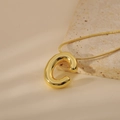 Close-up of golden bubble initial C pendant with a sleek snake chain on a neutral stone - Letter C Style (24WN028)