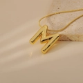 Macro detail of a 3D bubble M initial pendant necklace with a gold snake chain on marble - Letter M Style (24WN028)