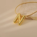 Close-up of golden bubble letter N pendant with sleek snake chain on a stone surface - Letter N Style (24WN028)