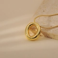 Detail shot of a chunky gold bubble letter pendant on a sleek snake chain over stone - Letter O Style (24WN028)