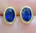 Ovale blaue Saphir Ohrstecker mit goldener Zargenfassung zur Präsentation auf der Hand - Ovale Zargenfassung Ohrstecker / Goldene Basis - Dunkelblauer Stein