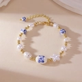 Close-up of blue floral porcelain beads and pearls with a golden lobster clasp detail - Oval Bead