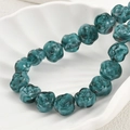 Macro shot of dark turquoise glass rose beads in a white shell dish for jewelry making - Peacock Green