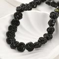 Detailed view of black glass rose beads with intricate petal textures in a white shell dish - Black