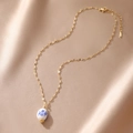 Detail of blue and white floral porcelain bead pendant with gold chain on silk fabric - Flat Round Style