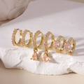 Close-up of gold plated huggie earrings set with pink cubic zirconia on white stone - 3 Pairs Set / Gold Pink