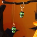 Dettaglio di orecchini a teschio asimmetrici per Halloween su rami scuri e arancio - Verde
