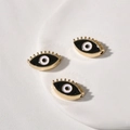 Makroaufnahme von drei vergoldeten Evil Eye Charms mit schwarzer Emaille auf Tablett - Augenform / 1 Stück (18.4x10.6x4.86mm) / Schwarz