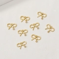 Makroaufnahme von 8 goldenen Schleifenanhängern mit Zirkonia auf beigem Hintergrund - 14K Gold Linke Kleine Schleife Stil