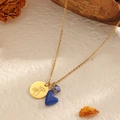 Goldene Edelstahlkette mit Blumenmedaillon und blauem Herzanhänger auf strukturiertem Hintergrund - Dezember