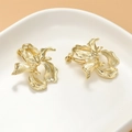 Detalle macro de pendientes de flores bañados en oro de 14k en un plato de cerámica blanca - Clip de oreja de flor dorada (1 pieza)