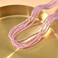 Nahaufnahme von 2mm facettierten rosa Katzenaugenperlen auf einem goldenen Tablett - Rosa
