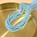 Detail von facettierten hellblauen 2mm Katzenaugenperlen auf einem goldenen Tablett für DIY - See Blau