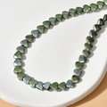 Detailed macro of 6mm faceted heart hematite beads with metallic luster on ceramic stand - 6# Green Faceted Heart (Approx. 70 Pcs/Strand)