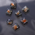 Macro detail of square resin charms with embedded gold foil and dried petals for DIY crafts - Black Base Orange Leaf