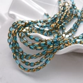 Macro shot of faceted lake blue oval glass beads with gold trim in a white ceramic dish - 50 Pieces Set / Teal