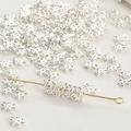 Macro shot of silver snowflake spacer beads on a gold metal needle for DIY jewelry making - Thick Silver Zircon Snowflake
