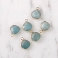 Close-up of faceted light blue water drop pendants with gold plated edges on marble - Gold Edged Amazonite