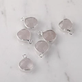Macro view of six pink crystal teardrop charms with silver metal borders on marble - Silver Edged Rose Quartz