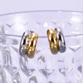 Macro detail of two-tone C-shaped hoop earrings hanging on a textured glass rim - Two-Tone Gold and Silver