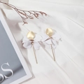 Close-up of white 3D flower petal earrings with gold dangling rods on soft white fabric - White