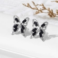 Macro shot of silver butterfly stud earrings with black crystals on white leather - Black (A1561)
