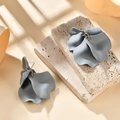 Macro shot of grey petal drop earrings on stone slabs with shadow highlights - Gray
