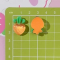 Dettaglio di ciondoli a carota in resina arancione con dimensioni su scala graduata verde - Carota