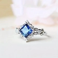 Macro shot of princess cut blue gemstone ring with intricate vine hollow-out metal details - US 5 / Blue