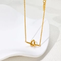 Detail view of 18K gold knot pendant necklace on white ceramic tray with soft shadows - Gold (B329)