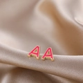 Macro shot of gold letter A stud earrings with pink enamel on champagne satin - Rose Red A