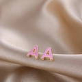 Macro shot of gold-plated letter A stud earrings with pink enamel on satin fabric - Pink A