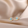 Detailed macro view of golden evil eye stud earrings with light blue enamel and small crystal - Blue Eye
