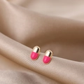 Detailed close-up of capsule-shaped stud earrings in gold and pink on champagne silk - Red Pill