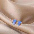 Detailed close-up of cute blue alien enamel stud earrings on luxury gold silk fabric - Blue Alien Head