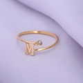 Minimalistische gouden ring met letter M en zirkonsteen op een paarse stoffen ondergrond - Goud-M